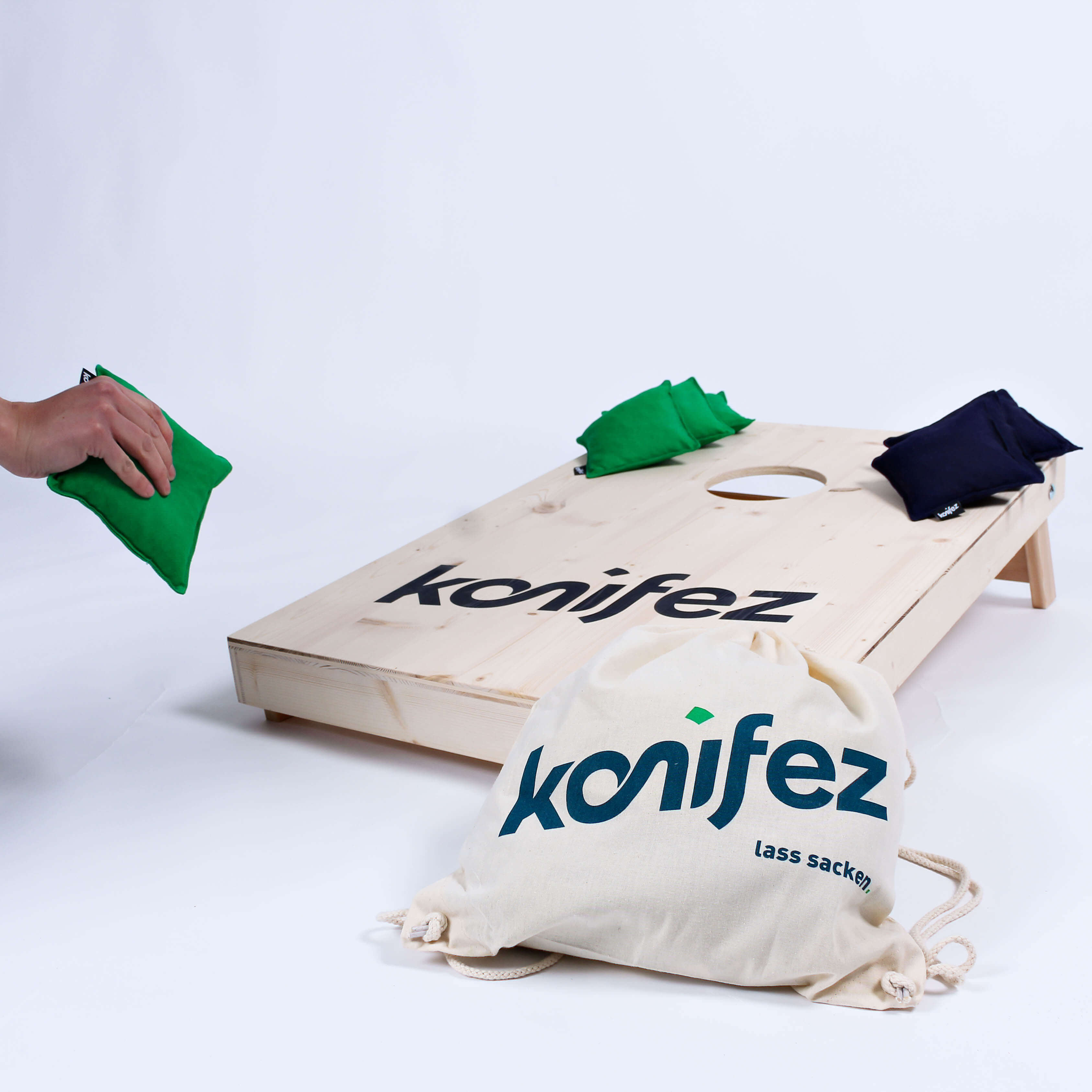 cornhole-konifez-spiel-gartenspiel-parkspiel-wurfspiel-hochzeitsspiel-event-kaufen-spielen-outdoor-produkt-4 Ein Hand wirft ein konifez-Säckchen auf ein Cornhole-Brett